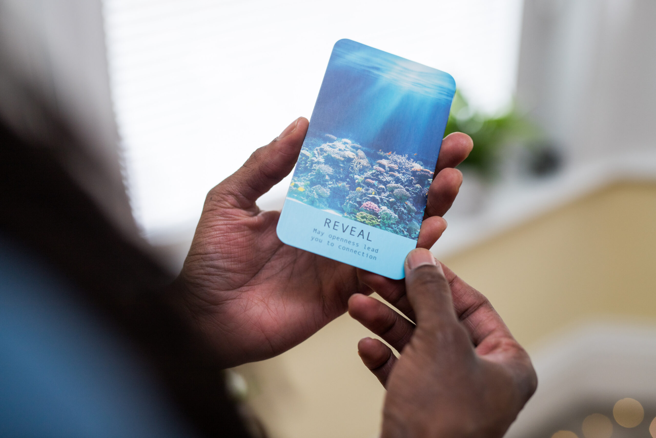 Man holdin the oracle card which reads: Reveal - May openness lead you to connection